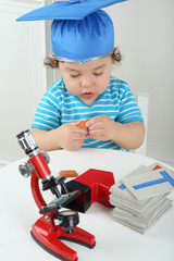 Small boy in blue graduation hat sitting at table with red microscope