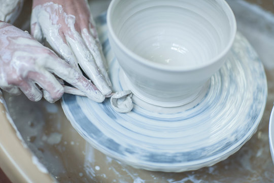 Close up of female potter's hands scraping clay bowl on pottery wheel in workshop