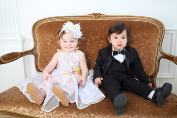 Beautiful little kids in costumes bride and groom sitting on couch
