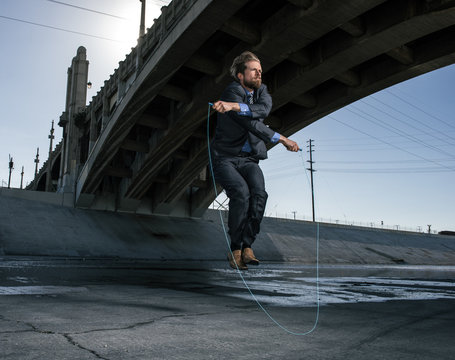 Businessman skipping, Los Angeles river, California, USA - Powered by Adobe