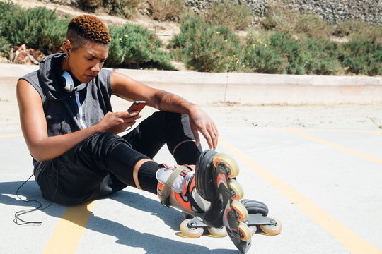 Woman wearing rollerblades and headphones sitting on floor looking at smartphone