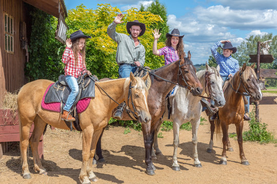 cowboy family of four on horses waving their hands