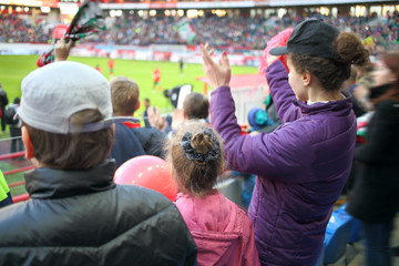 Obraz na płótnie Canvas Woman, girl and boy standing applause among fans at a sports stadium, the view from the back