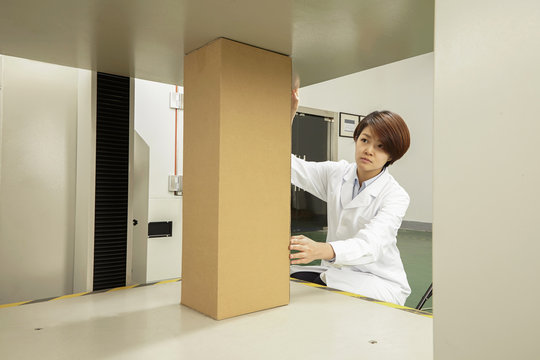 Female technician placing cardboard box on packaging machine in printing and packaging factory, China