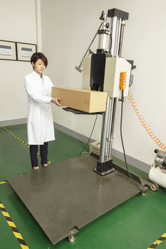 Female technician placing cardboard box on packaging machine in printing and packaging factory, China