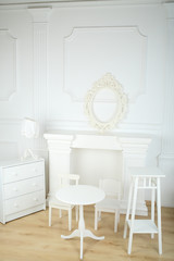 Interior white room with columns in ancient style, a fireplace and openwork frame, round table and chairs, commode and lamp