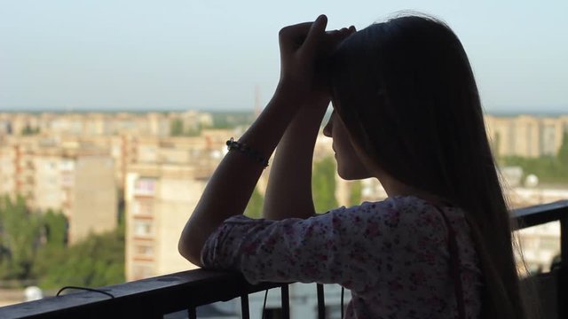 Depressed teenage girl. Silhouette of young woman in despair standing alone on balcony with view of city