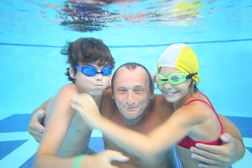 Portrait of grandfather with boy and girl under water in the swimming pool