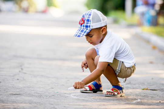 African American boy draws with chalk on the pavement