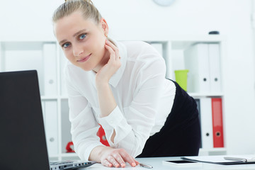 Portrait of a young  businesswoman standing next to a table with a laptop. Business, exchange market, job offer, analytics research, excellent education, certified public accountant concept.