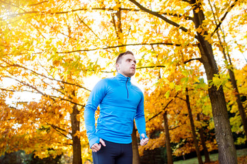 Young handsome athlete running outside in sunny autumn nature