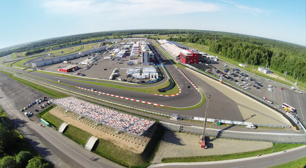 Sports cars passes by tribunes with people at summer sunny day. Aerial view (Photo with noise from action camera)