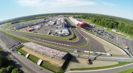 Sports cars passes by tribunes with people at summer sunny day. Aerial view (Photo with noise from...