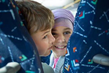 Two children are sitting in bus and turning back.
