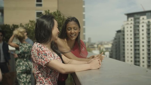  Happy female friends chatting & looking at view at rooftop party