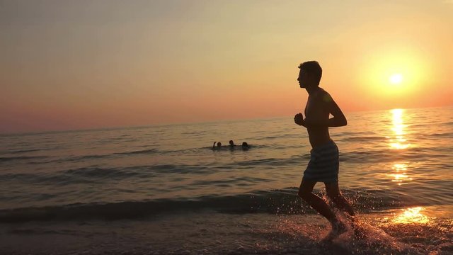 Young man with headphones run at sea at sunrise. 