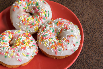 Three white frosted cake donuts with colorful sprinkles
