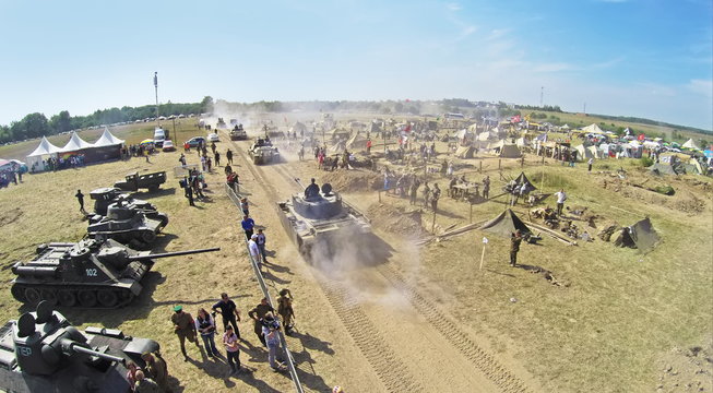 Tanks ride near military camp with many people during reconstruction Battlefield at Second World War. Aerial view (Photo with noise from action camera)