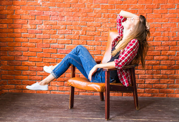 Cute woman with long legs sitting in the armchair behind a brick wall