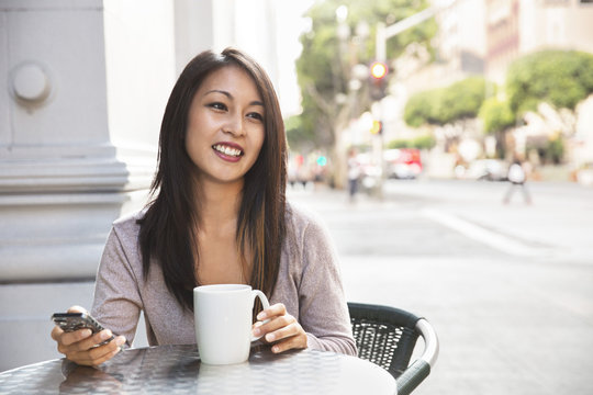 Woman with cell phone enjoying coffee at sidewalk cafe