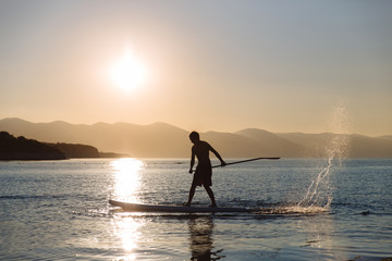 silhouette of young boy paddle boarding at sunset. concept  lifestyle sport