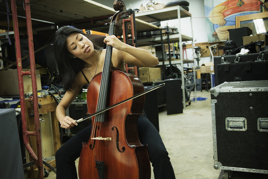 Asian woman playing cello in warehouse
