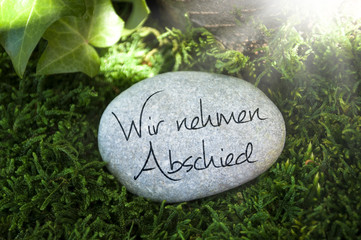 Stein auf Moos mit Efeu und Trauerspruch Wir nehmen Abschied