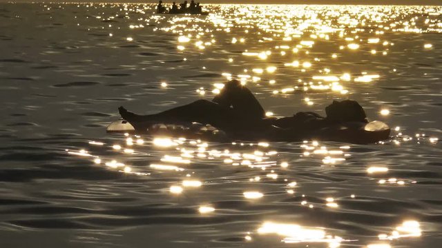 Woman in bikini floating on inflamable mattress on the sea sunset