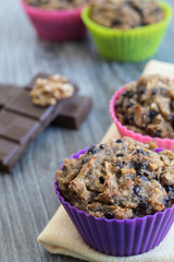 Fruit muffins on a yellow napkin and a grey wooden table. Walnuts, chocolate and two out of focus muffins in the background.