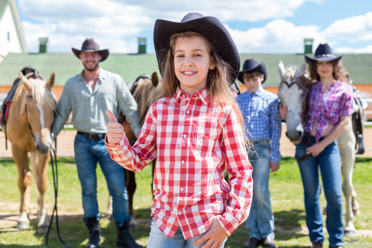 cowboy girl with ok gesture closeup portrait on background of her family with horses