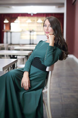 Beautiful woman with long hair in a green evening dress sitting at a table in a cafe