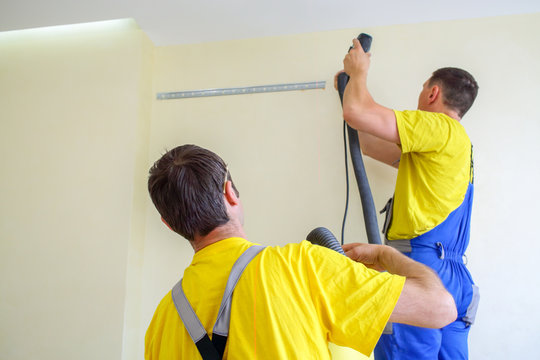 two male furniture assemblers in uniform drill walls with a vacuum cleaner
