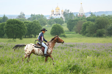 A man in a hat riding a spotted horse on the field on the basis of equestrian tourism Avanpost