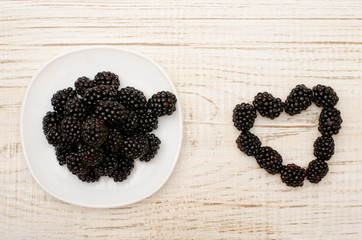 Saucer with blackberries, blackberry heart, light wood table