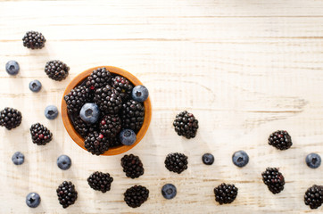 Fototapeta na wymiar Blackberries and blueberries in a wooden glass on a light wooden background