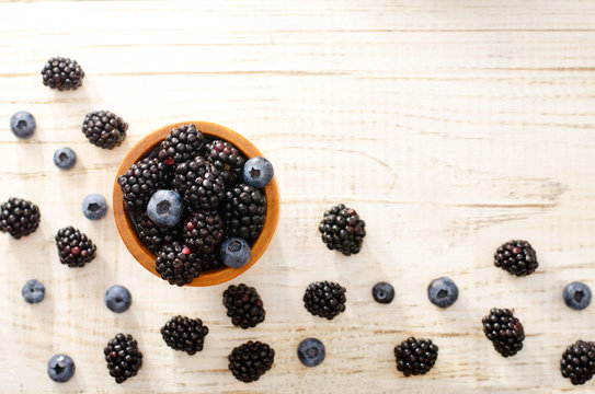 Blackberries and blueberries in a wooden glass on a light wooden background