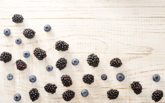Blackberries and blueberries in a corner of the frame, on a light wooden background