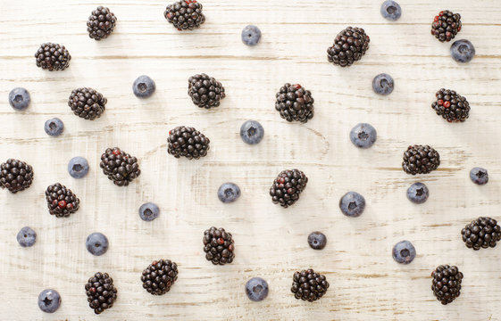 Blueberries and blackberries fill light wooden background
