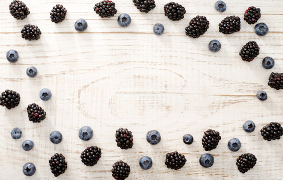 Oval frame with blueberries and blackberries on a light wooden background