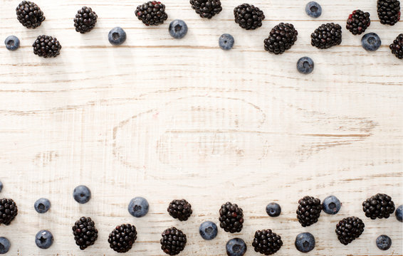 Framing of blueberries and blackberries on a light wooden background