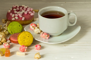 Cup of tea on wooden background with popcorn macaron donut