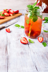 Homemade delicious strawberry compote in glass jar on white wooden table. Healthy food concept with copy space.