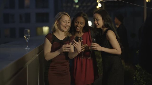  Happy female friends pose to take a selfie at summer rooftop party
