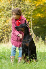 Little curly girl and dobermann are looking to the right in park, focus on a dog.