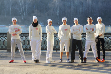 Group of seven young men in white shirts and hats stand in line on waterfront