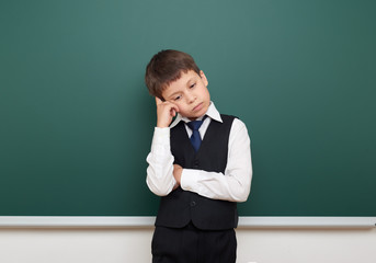school student boy posing and think at the clean blackboard, grimacing and emotions, dressed in a black suit, education concept, studio photo