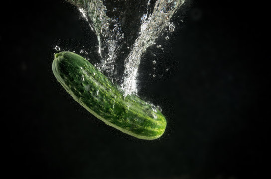 Fresh Cucumber with water splash on black background with air bubbles.
