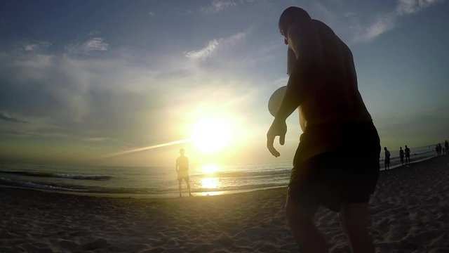 Two guys playing Frisbee together in shorts at sea sunset
