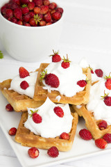 waffles with wild strawberries and whipped cream on white table