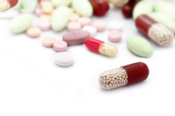 Medical capsule and colored pills blurred in background, isolated on white